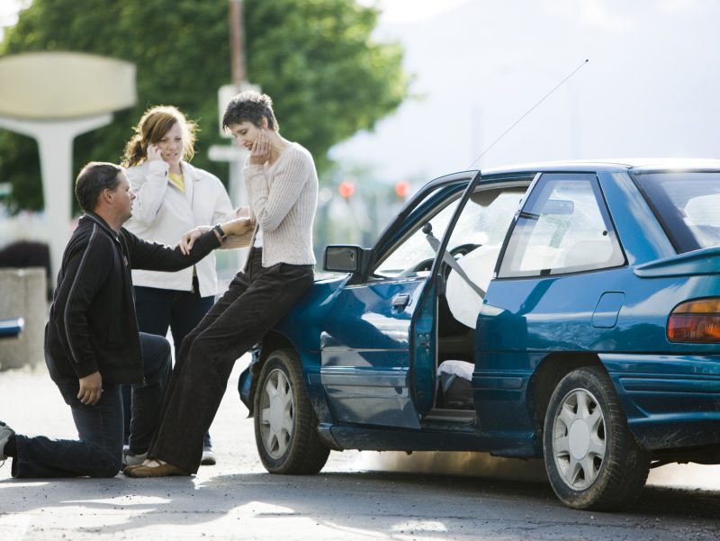 A man is on one knee comforting a woman after a car accident